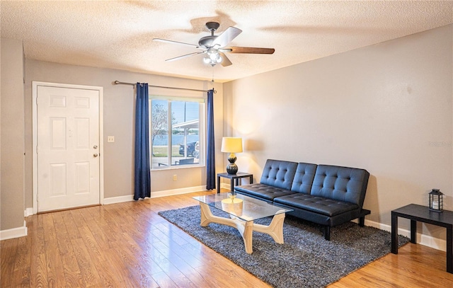 living area featuring a textured ceiling, baseboards, a ceiling fan, and wood finished floors