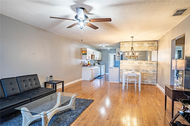 living room with visible vents, ceiling fan with notable chandelier, a textured ceiling, and light wood-type flooring