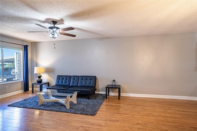 living room with ceiling fan, baseboards, a textured ceiling, and wood finished floors