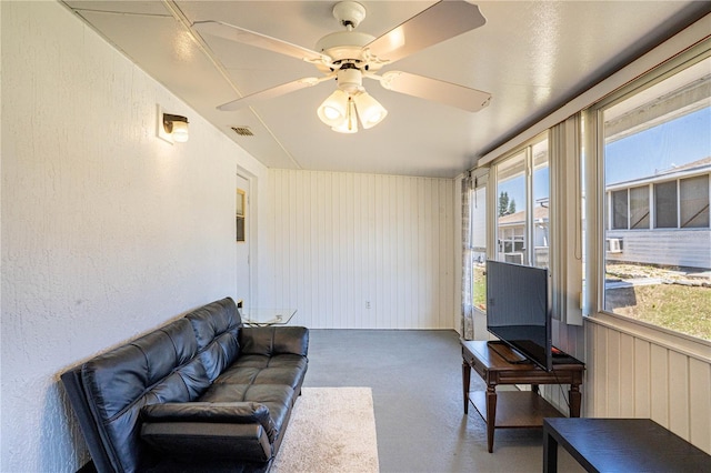 living room featuring a textured wall, visible vents, carpet floors, and ceiling fan