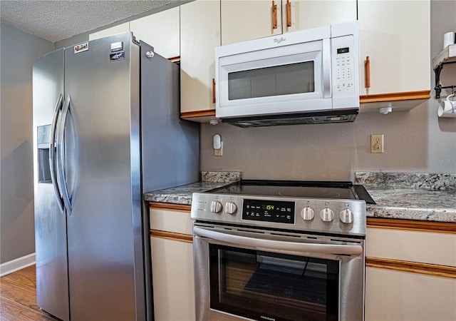 kitchen with light stone counters, light wood-style flooring, stainless steel appliances, white cabinets, and a textured ceiling