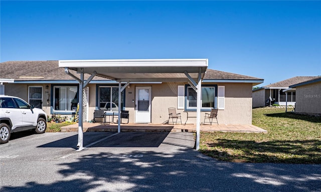 view of front of home with covered and uncovered parking, a patio, a front lawn, and a shingled roof