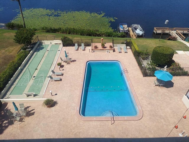 community pool with a patio, fence, a yard, a water view, and shuffleboard