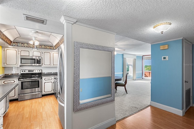 kitchen with dark countertops, visible vents, light wood finished floors, ornamental molding, and appliances with stainless steel finishes