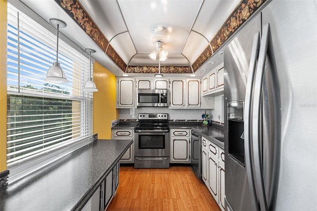 kitchen featuring decorative light fixtures, a tray ceiling, dark countertops, wood finished floors, and appliances with stainless steel finishes