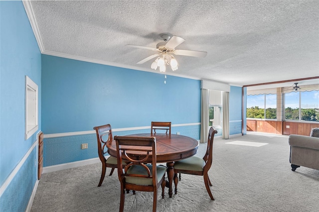 carpeted dining space with a wainscoted wall, a textured ceiling, crown molding, and a ceiling fan