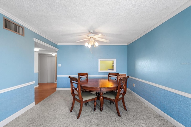 dining room with a ceiling fan, visible vents, wallpapered walls, crown molding, and carpet flooring