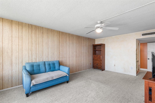 living area with visible vents, carpet, ceiling fan, wood walls, and a textured ceiling