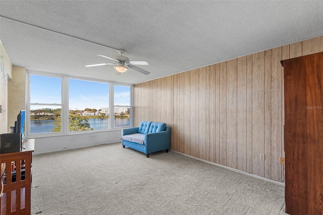 living area with wooden walls, ceiling fan, a water view, carpet floors, and a textured ceiling