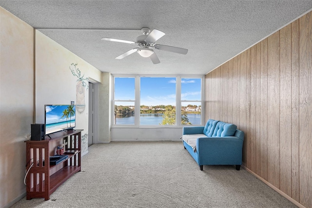 sitting room featuring a textured ceiling, wooden walls, ceiling fan, and carpet