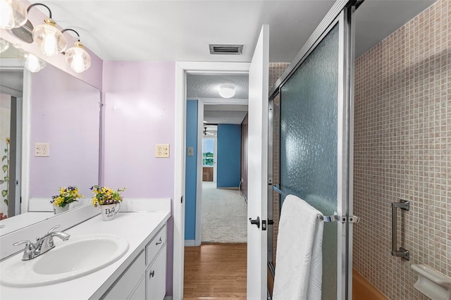 full bathroom featuring vanity, wood finished floors, visible vents, and a shower with shower door