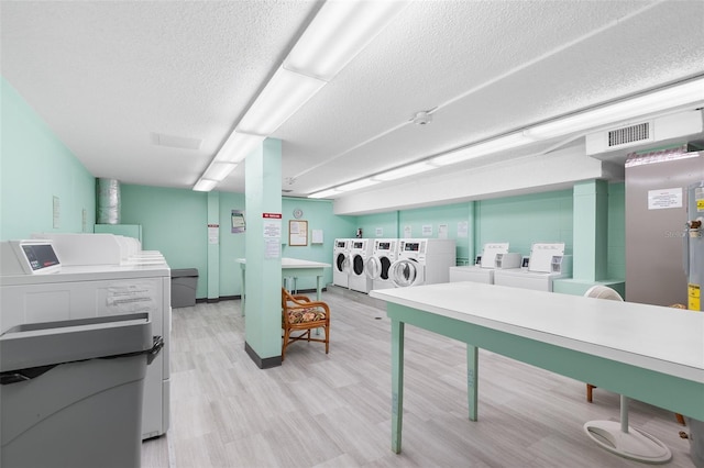 common laundry area with light wood finished floors, visible vents, washer and dryer, and a textured ceiling