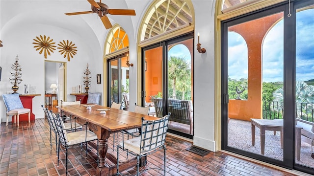 dining room with visible vents, brick floor, baseboards, ceiling fan, and vaulted ceiling