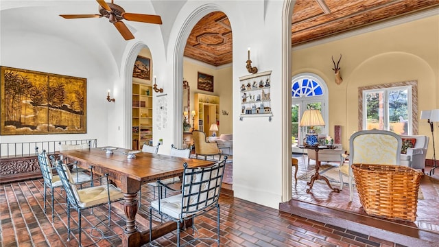 dining area featuring ceiling fan, ornamental molding, a high ceiling, brick floor, and arched walkways