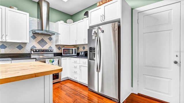 kitchen featuring backsplash, white cabinetry, stainless steel appliances, butcher block counters, and wall chimney range hood