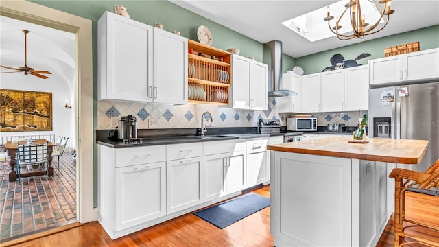 kitchen featuring open shelves, a sink, appliances with stainless steel finishes, wall chimney exhaust hood, and butcher block counters