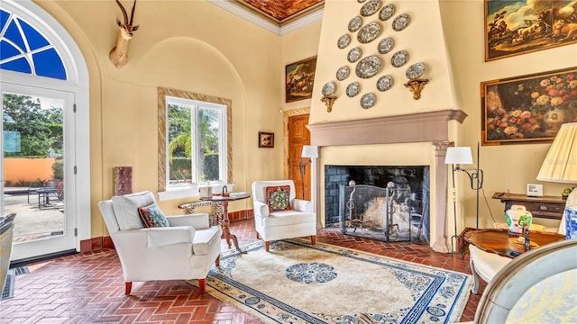 living area featuring baseboards, brick floor, ornamental molding, a towering ceiling, and a large fireplace