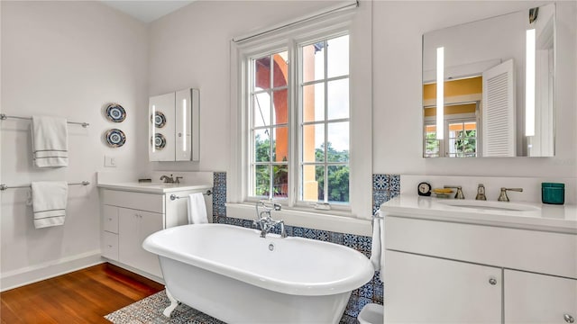 full bathroom featuring a freestanding tub, two vanities, wood finished floors, and a sink