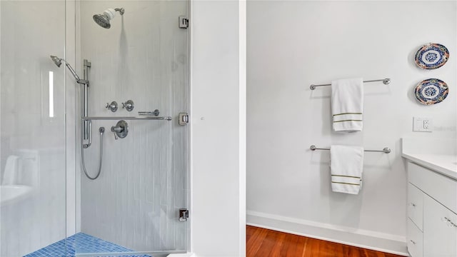 full bath featuring baseboards, vanity, wood finished floors, and a shower stall