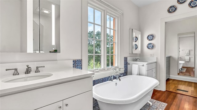 full bath featuring hardwood / wood-style floors, a soaking tub, two vanities, and a sink