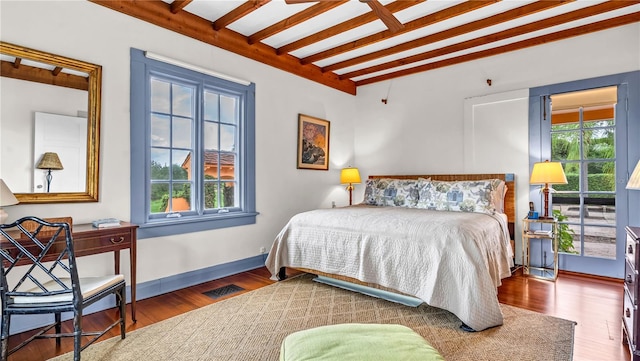 bedroom with beamed ceiling, wood finished floors, visible vents, and baseboards