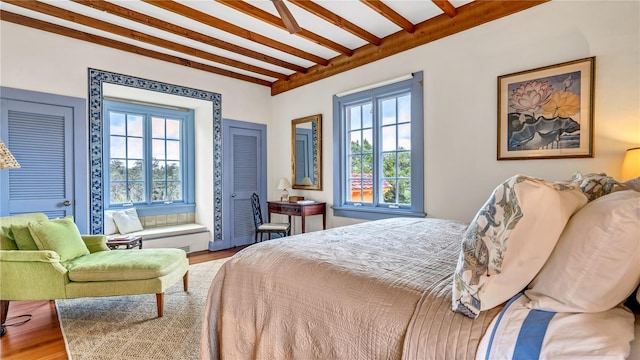 bedroom featuring beam ceiling, multiple windows, and wood finished floors