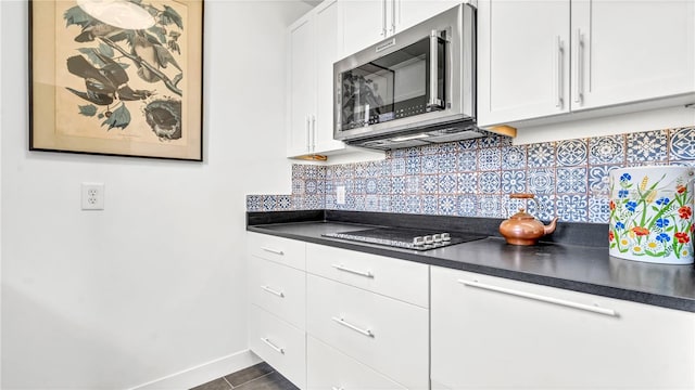 kitchen featuring black electric cooktop, stainless steel microwave, dark countertops, white cabinetry, and decorative backsplash