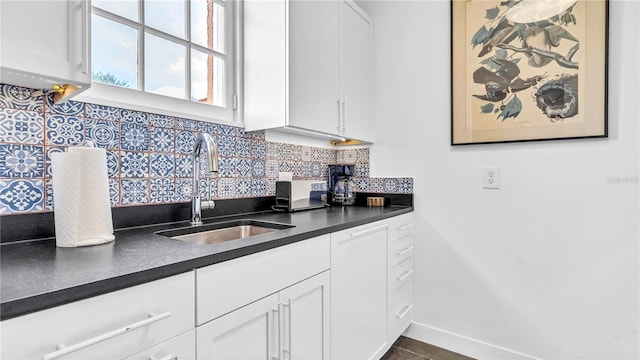 kitchen featuring dark countertops, white cabinets, backsplash, and a sink