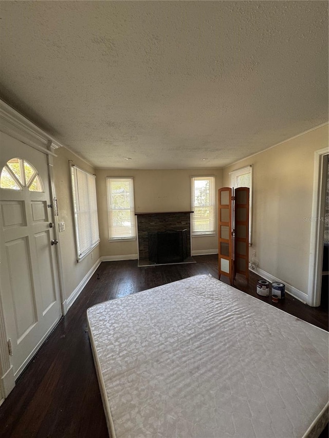 unfurnished living room featuring a fireplace with flush hearth, a textured ceiling, baseboards, and dark wood-style flooring