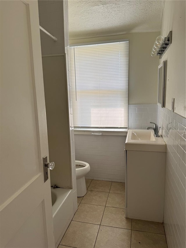 bathroom with tile patterned floors, toilet, a textured ceiling, tile walls, and vanity