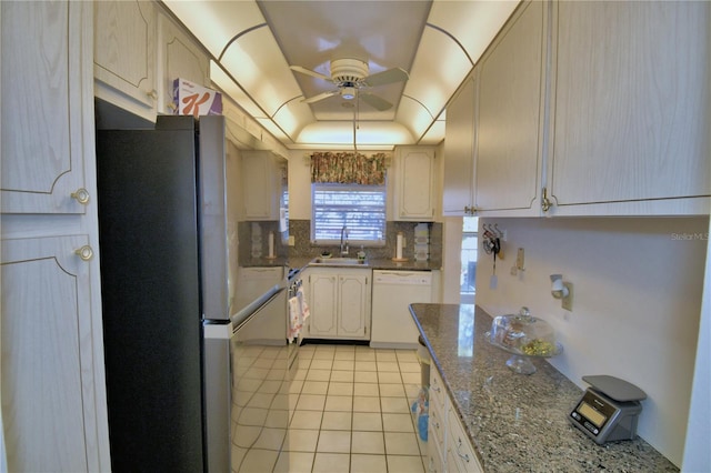 kitchen with a sink, a tray ceiling, freestanding refrigerator, dishwasher, and ceiling fan