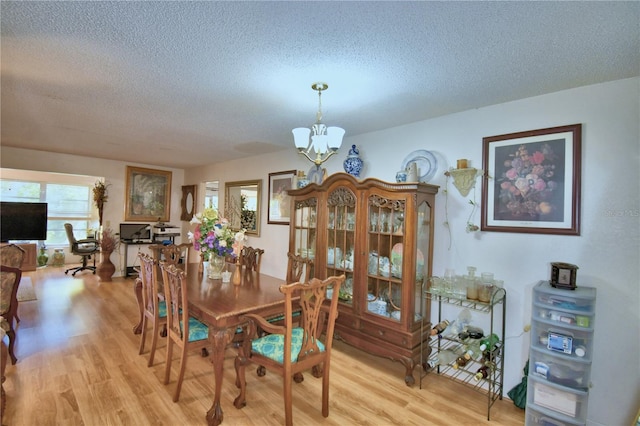 dining space with a notable chandelier, a textured ceiling, and light wood-style floors