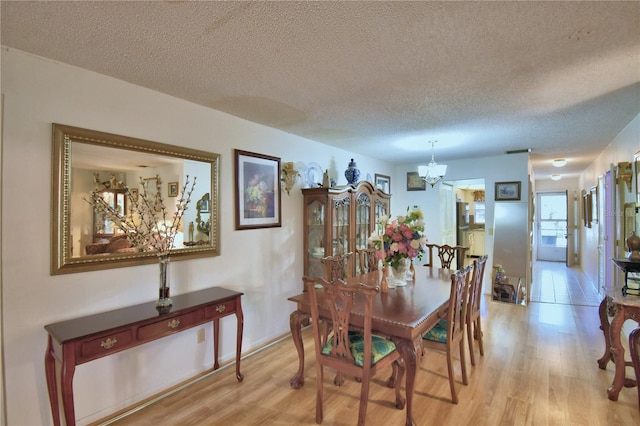 dining room featuring a notable chandelier, light wood finished floors, and a textured ceiling