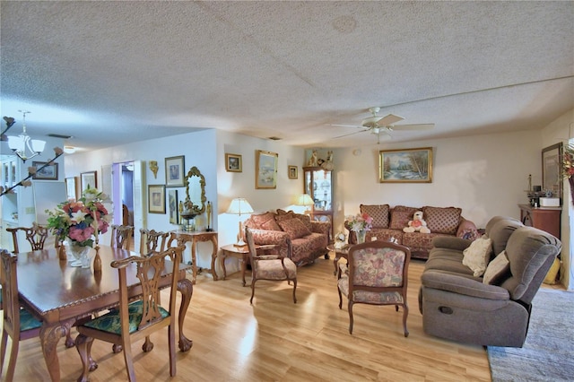 living room with ceiling fan with notable chandelier, light wood-style flooring, and a textured ceiling