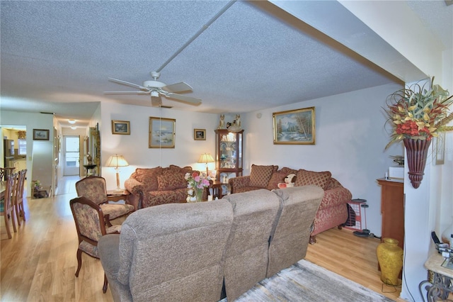 living room with a textured ceiling, light wood-style floors, and a ceiling fan