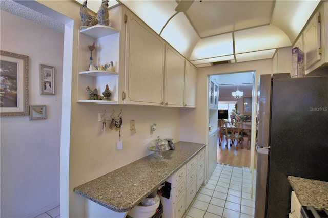 kitchen with open shelves, stone countertops, light tile patterned flooring, and freestanding refrigerator