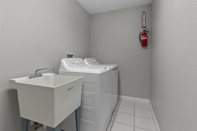 clothes washing area with independent washer and dryer, a sink, light tile patterned floors, baseboards, and laundry area