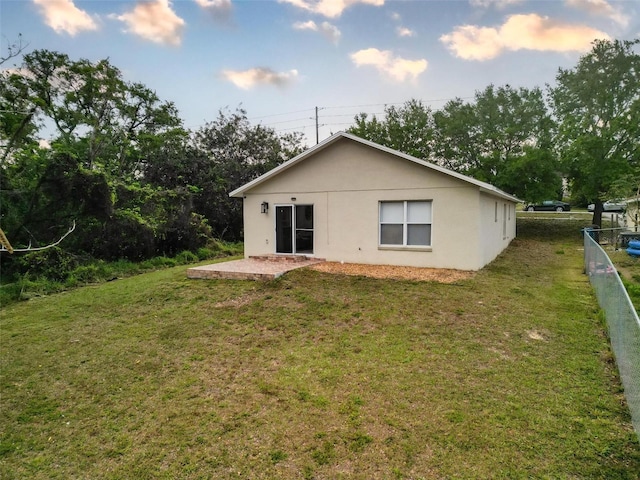 back of house with stucco siding, a patio, a yard, and fence