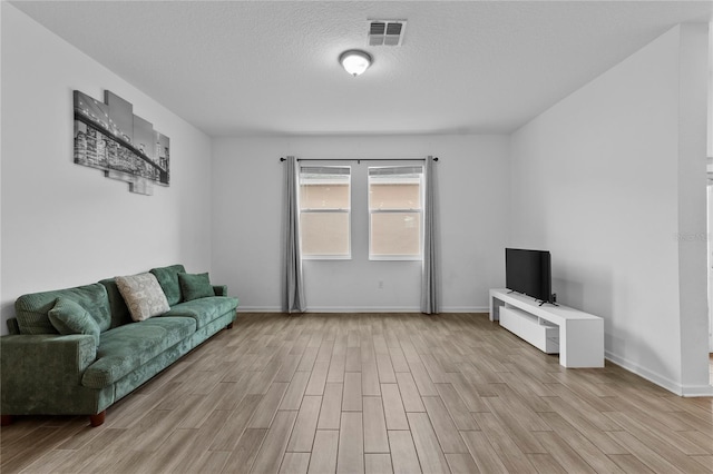 living area with visible vents, light wood-style flooring, a textured ceiling, and baseboards