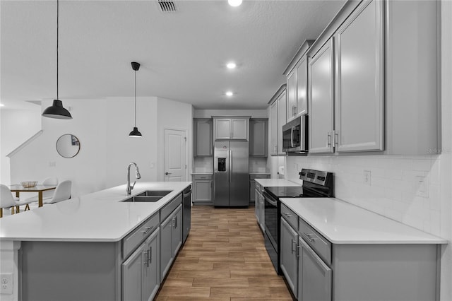 kitchen with gray cabinetry, a sink, light wood-style floors, appliances with stainless steel finishes, and decorative backsplash