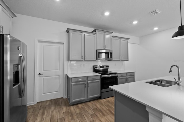 kitchen featuring a sink, backsplash, gray cabinetry, stainless steel appliances, and dark wood-style flooring