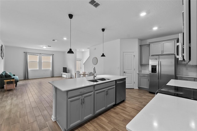 kitchen featuring visible vents, gray cabinetry, open floor plan, appliances with stainless steel finishes, and a sink