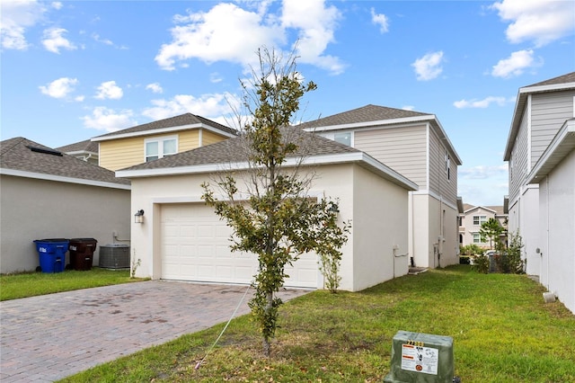 view of front of home featuring a front lawn, stucco siding, central AC unit, decorative driveway, and a garage