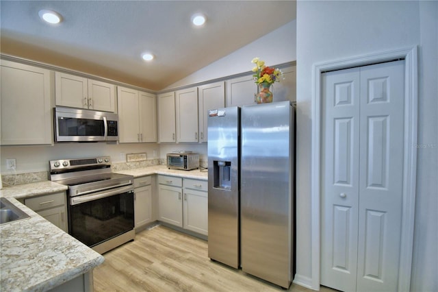 kitchen with light wood-type flooring, light countertops, vaulted ceiling, recessed lighting, and appliances with stainless steel finishes