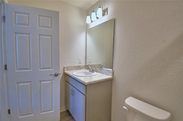 half bath featuring vanity, toilet, and a textured wall