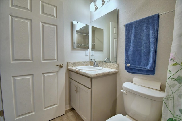 bathroom with toilet, vanity, a textured wall, and wood finished floors