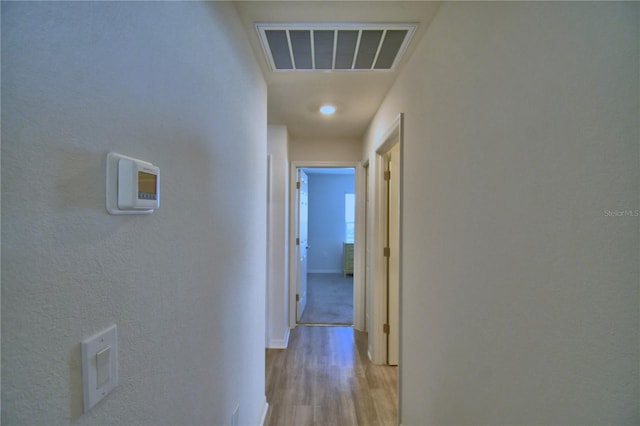 hall with visible vents, baseboards, and light wood-style flooring