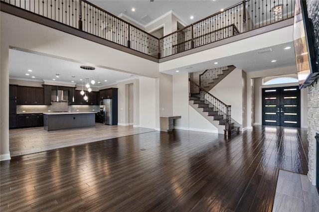 living area featuring light wood-style floors, crown molding, baseboards, a towering ceiling, and stairs