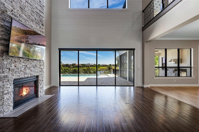 unfurnished living room with wood finished floors, baseboards, ornamental molding, a stone fireplace, and a towering ceiling