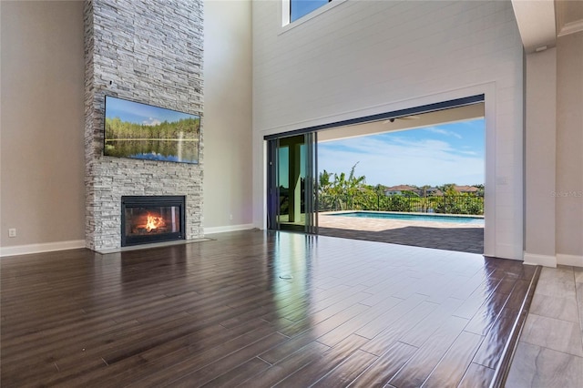 unfurnished living room featuring a towering ceiling, a fireplace, baseboards, and wood finished floors